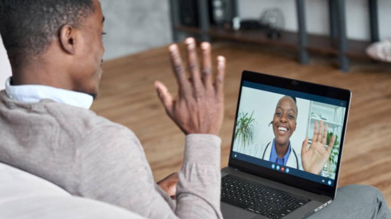 Male black patient talking on conference video call to female african doctor. Virtual therapist consulting young man during online appointment on laptop at home. Telemedicine chat, telehealth meeting stock photo