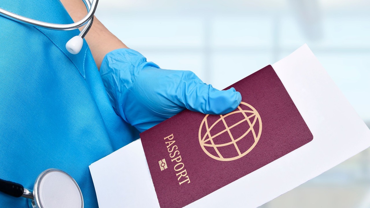 A gloved clinician holds a passport on a blank form beside a stethoscope.