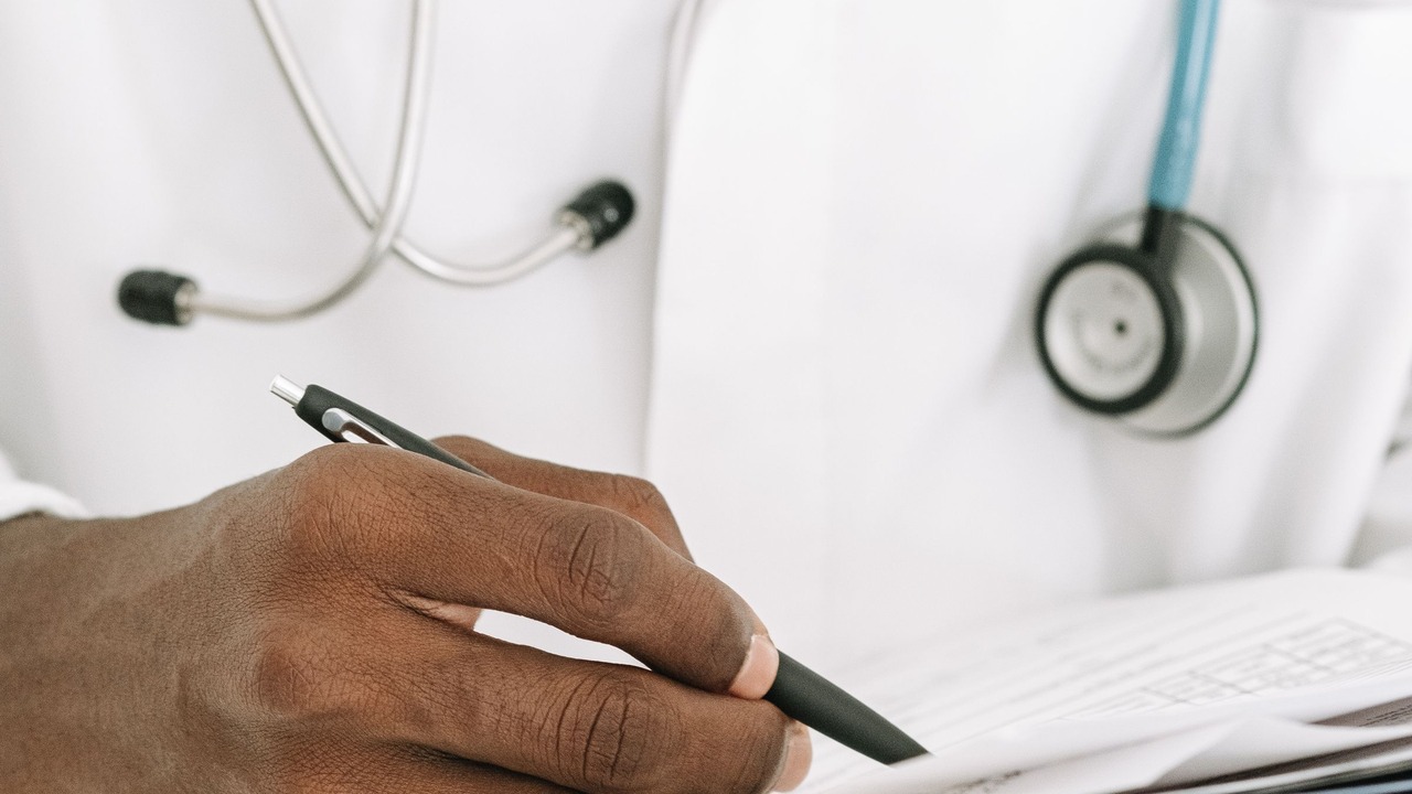 A doctor fills in a form beside a stethoscope.
